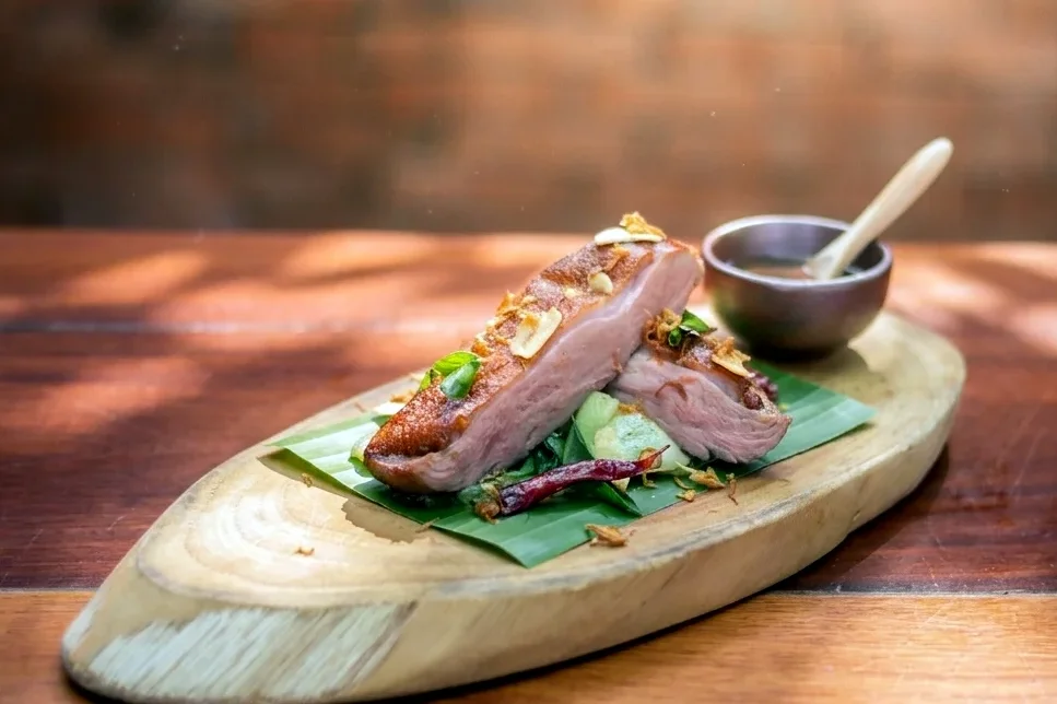 Sliced roast duck on a banana leaf with a dipping sauce
