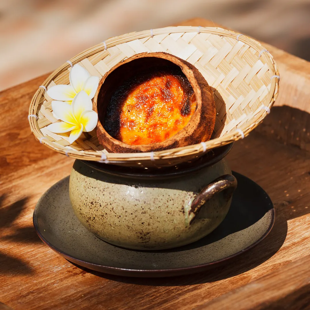 Cr&egrave;me br&ucirc;l&eacute;e caramelised in a coconut shell, served with a frangipani flower