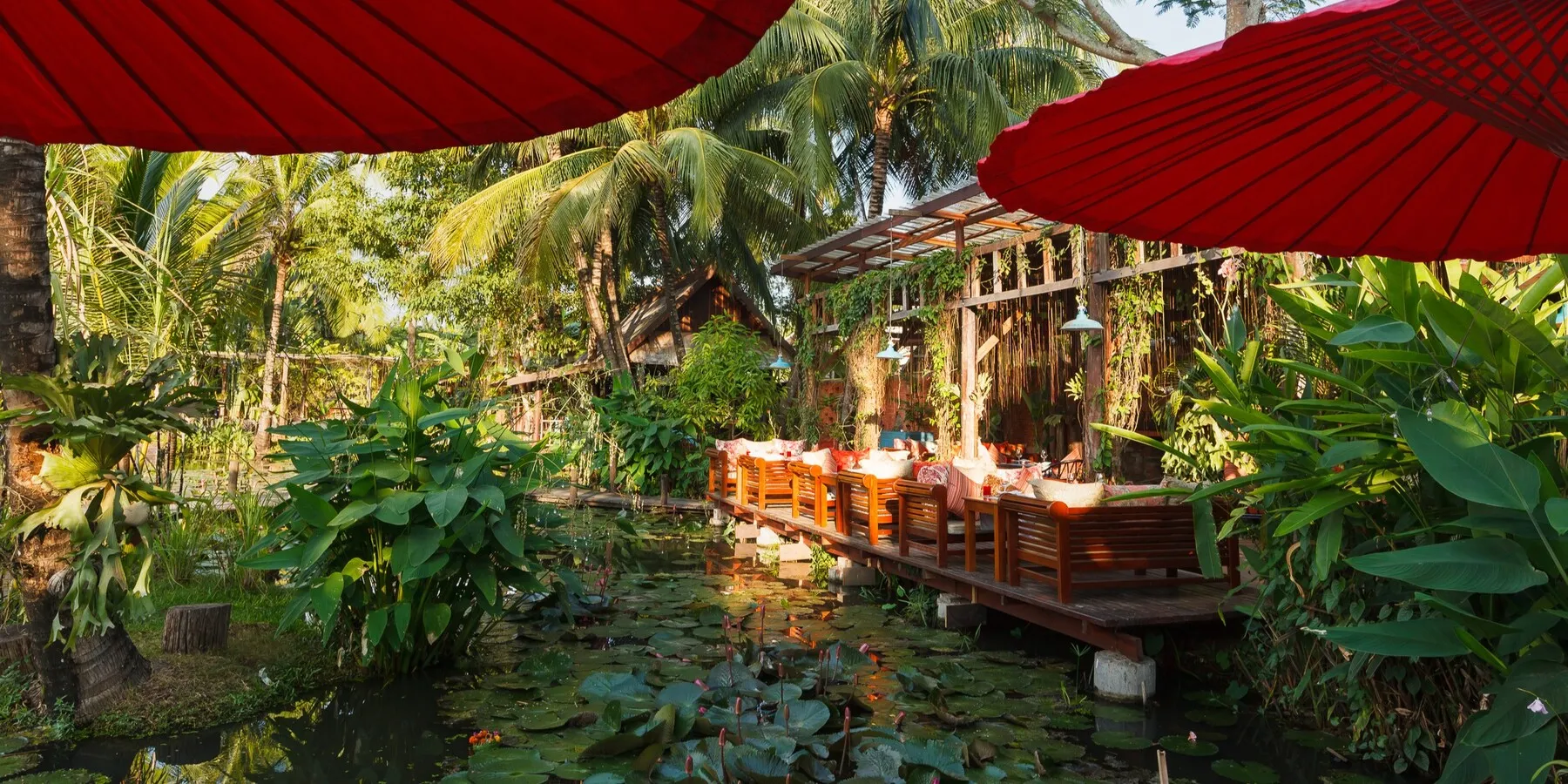 Red Lao parasols above the lily ponds at Manda de Laos, lounge seating along the walkway
